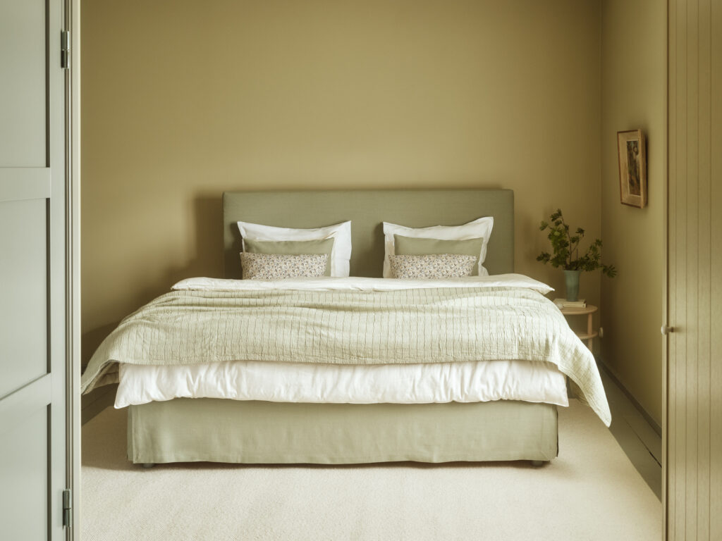 Das Aurea Continental-Bett, stilvoll gedeckt in Lino Green-Tönen, mit der Aava-Tagesdecke in Grün.
