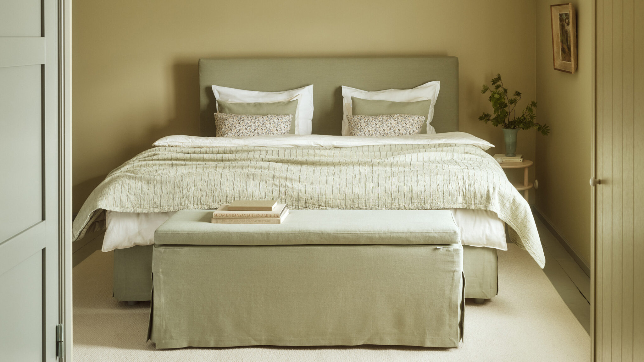 Matri Boxspringbett in Salbeigrün mit schlichtem Kopfteil, weißen und grünen Kissen und voluminöser, weißer Bettdecke im Schlafzimmer.