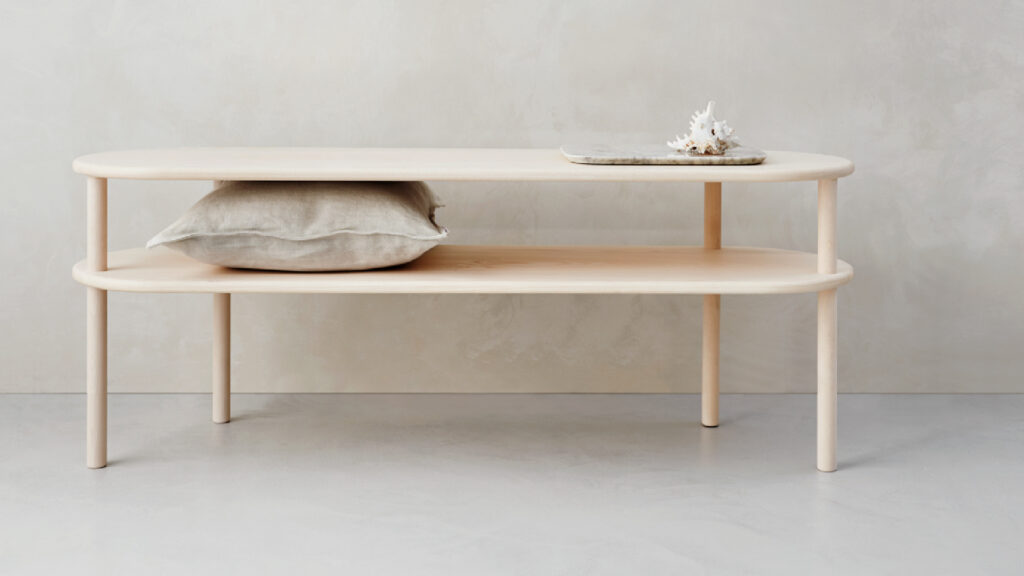 Heller, ovaler Matri Bettbank aus Holz mit zwei Ablageflächen, einem Leinenkissen und einem Dekorationselement auf der Oberseite.