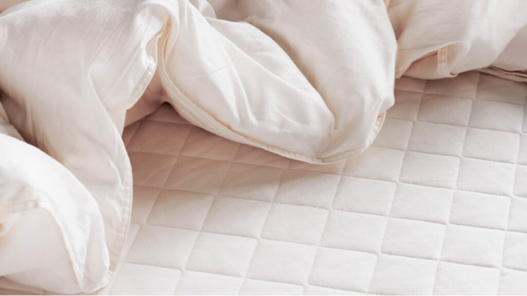 Detailaufnahme eines gesteppten Matri Toppers mit einer lockeren, hellen Bettdecke.